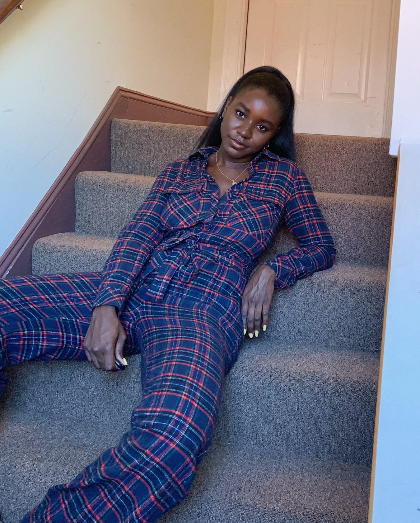 black girl wearing grunge blue and purple plaid utility jumpsuit on carpet stairs in hallway